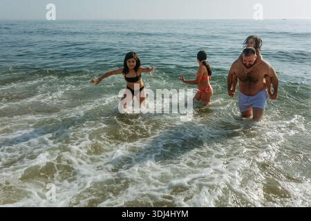 Hochwinkelansicht eines Vaters mit 3 Kindern, die mit Wellen spielen und Spaß haben Stockfoto