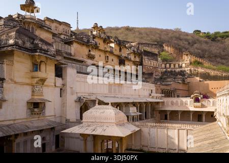 Bundi, Indien - 20. März 2022: Das Bild zeigt mehrere Ebenen von Palastgebäuden im Garh Palace mit kunstvollen architektonischen Details, mit Blick auf einen Hügel mit Festungsmauern im Hintergrund. Stockfoto