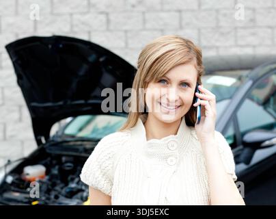 Ein dunkler Pkw mit erhöhter Motorhaube, der den Motorraum freilegt, befindet sich auf einem gepflasterten Parkplatz. Frau, Outdoor, mobil, offen, Lifestyle, Stadtverkehr, Fahrzeuge Stockfoto