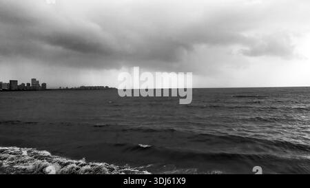 Dramatischer Monsunregen über dem Arabischen Meer mit dunklen Sturmwolken und der fernen Skyline Mumbais, schwarz-weiße Küstenlandschaft. Stockfoto