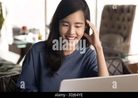 Fröhliche junge asiatische Freelancerin, die am Laptop arbeitet Stockfoto