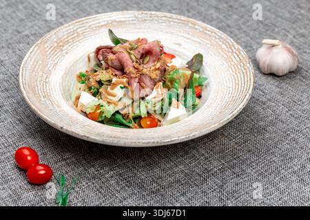 Eine Nahaufnahme eines köstlichen warmen Salats, serviert auf einer strukturierten Keramikplatte. Es enthält Scheiben von gekochtem Rindfleisch, gemischten Salatblättern, che Stockfoto