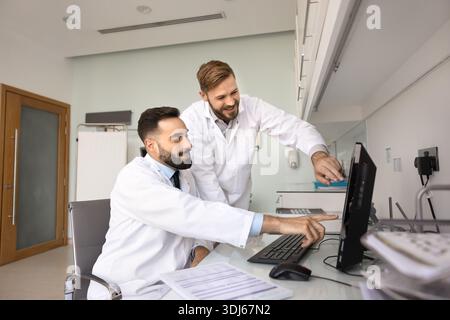 Zwei junge Ärzte zeigen mit Lächeln auf den Desktop-Monitor Stockfoto