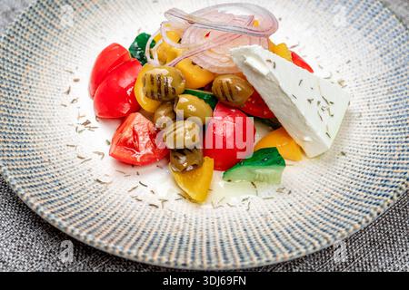 Eine lebendige Nahaufnahme eines traditionellen griechischen Salats, serviert auf einer strukturierten Keramikplatte. Es enthält frische Zutaten: Tomatenwürfel, Gurken, sl Stockfoto