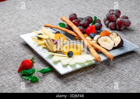 Eine wunderschön angeordnete Gourmet-Käseplatte mit verschiedenen Käsesorten, roten Trauben, frischen Erdbeeren, Heidelbeeren, Physalis, und dri Stockfoto