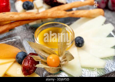 Nahaufnahme eines eleganten Vorspeisenaufstrichs mit einer Vielzahl von in Scheiben geschnittenen Hart- und Weichkäsesorten, begleitet von Heidelbeeren, Physalis-Früchten und getrockneten roten Beren Stockfoto