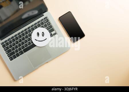 Kundenbewertungen zur Online-Bewertung von Laptops, Smiley-Gesichtssymbol für digitale Zufriedenheitsumfrage, Telefongerät neben modernen Komp Stockfoto