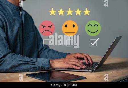 Kundenfeedback und Kundenzufriedenheitsumfrage zeigen, dass ein Mann mit seinem Laptop eine Bewertung mit einem Lächeln abgibt, das die Bedeutung des Kunden unterstreicht Stockfoto