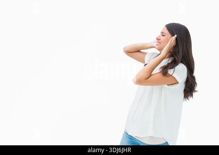 Die Frau bedeckt beide Ohren und grimmt vor weißem Studio-Hintergrund, Kopierraum. Highkey, minimalistisch, Spannung, Rauschen, Beleuchtung, Lager, Branding Stockfoto