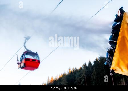 Beschneiungsmaschine, die während der Wintersaison Kunstschnee erzeugt, in einem Bergskigebiet, wobei die Seilbahn über dem Berg vorbeifährt. Konzept der Skiindustrie, Stockfoto