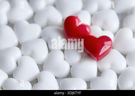 Zwei leuchtend rote Herzen stehen inmitten eines Meeres aus weißen Herzen, die Liebe und Einzigartigkeit symbolisieren Stockfoto