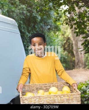 Afroamerikanisches Kind, das einen Korb mit Zitronen auf dem Weg neben dem Van hält und Senfhemd trägt. Kind, Zitrusfrüchte, Obst, Outdoor, Garten, Sonnenlicht, gewebt Stockfoto