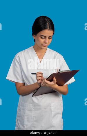 Junge Frau in weißer Uniform mit Klemmbrett und Schreiben, im Gesundheitswesen tätig Stockfoto