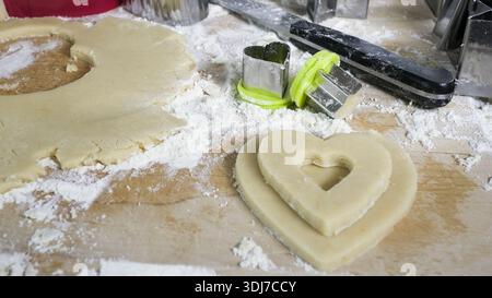 Zubereitung hausgemachter herzförmiger Kekse mit Teig, Mehl und Schneiden auf einem Holzbrett Stockfoto