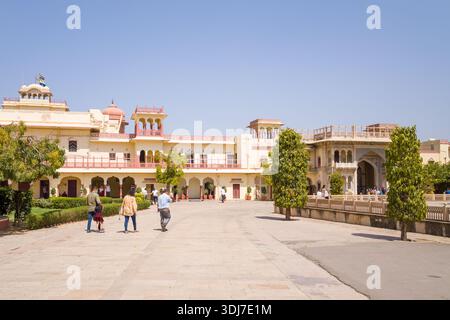 Jaipur, Indien - 16. März 2022: Der Innenhof des Stadtpalastes wird mit mehreren Besuchern zu Fuß gezeigt, getrimmte Bäume, gelb gestrichene historische Gebäude, Balkone, bogenförmige Eingänge, und ein klarer blauer Himmel. Stockfoto