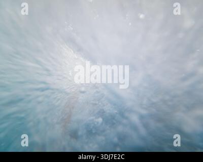 Starker Wasserstrahl unter Wasser mit Luftblasen, der dynamische weiße Schaumstruktur und turbulenten abstrakten blauen aquatischen Hintergrund erzeugt. Stockfoto