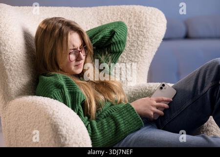 Junge Frau, die sich unwohl fühlt, während sie ihr Smartphone hält, Schmerzen oder Belastung nach der Verwendung des Bildschirms spürt. Stockfoto