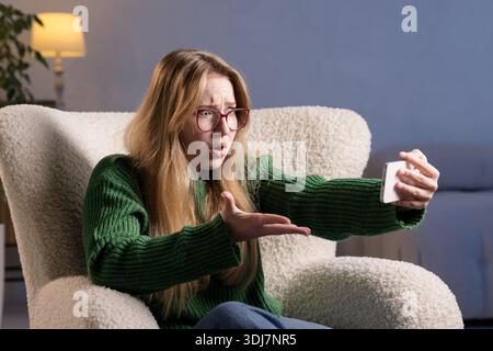 Wütende junge Frau, die während eines Videoanrufs telefoniert und Frustration und Enttäuschung über schlechte Nachrichten ausdrückt. Stockfoto
