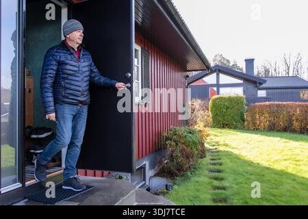 Mann in Winterkleidung steht am Hauseingang, betritt einen üppigen Garten mit Schatten und zeigt eine ruhige Umgebung im Freien Stockfoto
