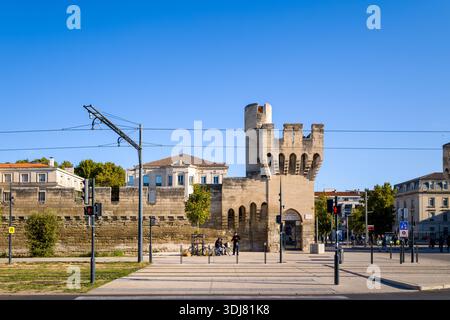 Avignon, Frankreich - 21. September 2022: Ein mittelalterliches Stadttor aus Stein und eine befestigte Mauer sind mit Straßenbahnlinien, Ampeln, Fußgängern und umliegenden Gebäuden unter einem klaren blauen Himmel zu sehen. Stockfoto