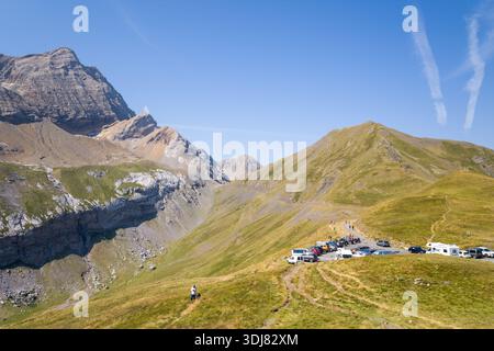 Parken dans les montagnes des Pyrenäes, Frankreich - 7. August 2022: Auf einem grasbewachsenen Bergrücken, umgeben von hohen Gipfeln unter klarem blauem Himmel, ist ein Parkplatz mit mehreren Autos, Lieferwagen und Menschen zu sehen. Stockfoto