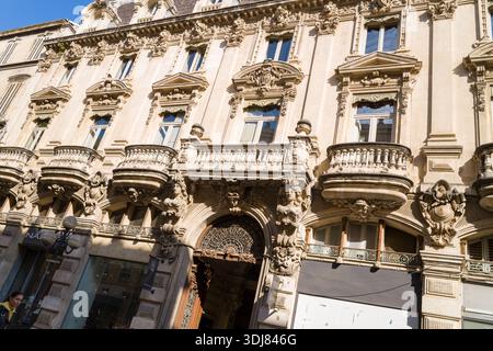 Avignon, Frankreich - 21. September 2022: Das Bild zeigt die detaillierte Fassade eines historischen Steingebäudes mit verzierten Balkonen, Skulpturen, Bogenfenstern und dekorativen architektonischen Elementen unter Sonnenlicht. Stockfoto