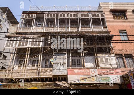 Delhi, Indien - 13. März 2022: Ein altes mehrstöckiges Gebäude mit verzierten Balkonen, Fensterläden und dekorativen Gitterleisten ist auf dem Sadar Basar zu sehen, mit zahlreichen Überdachungsdrähten und einem Schild der Union Bank, das unter klarem Himmel im Erdgeschoss zu sehen ist. Stockfoto