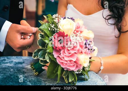 Hochzeitsstrauß in den Händen der Braut und des Bräutigams: Rosa Rosen, Gerberas und zarte weiße Blumen Stockfoto