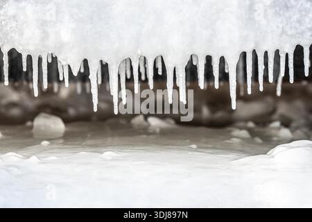 Eiszapfen hängen an einem kalten Winter- oder Frühlingstag auf einer gefrorenen Oberfläche Stockfoto