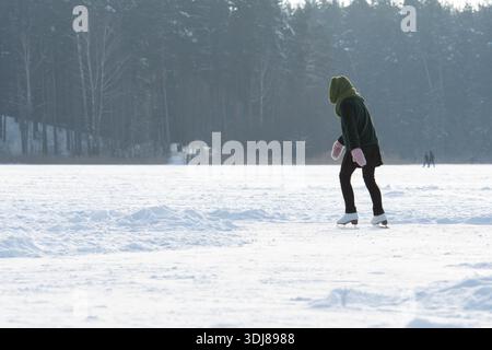 Mädchen Schlittschuhlaufen im Freien, die weiße Eisfiguren zeigen, die im Winter über schneebedecktes Eis mit einem Frost im Hintergrund gleiten Stockfoto