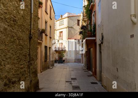 Unbekannte Lage - 19. Juni 2022: Blick auf eine enge Straße mit Wohngebäuden mit Balkonen mit Pflanzen und Blumen, Fensterläden und strukturierten Fassaden unter klarem blauen Himmel. Stockfoto