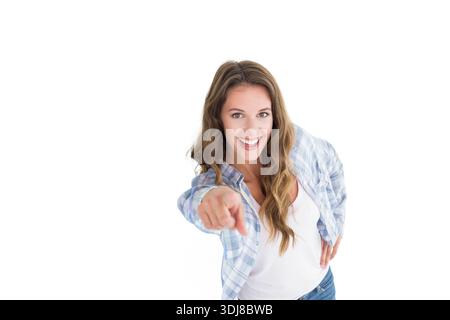 Frau lächelt und lehnt sich nach vorne, während sie mit dem Finger auf den Zuschauer im Studio mit kariertem Hemd zeigt. Porträt, Frau, Gesten, selbstbewusst, weiß, bac Stockfoto