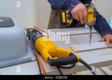 Der Zimmermann bohrt in Holz, während er in der Werkstatt die Säge auf dem Arbeitstisch verwendet Stockfoto