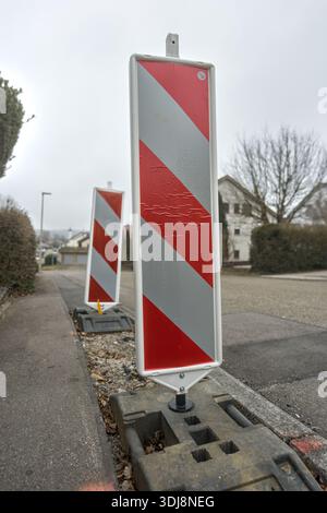 Zwei rot-weiße Bauschilder stehen auf einer grauen Straße unter bewölktem Himmel in einer städtischen Umgebung. Stockfoto