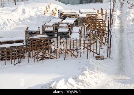 Schneebedeckte Holzgerüste, die nach starkem Schneefall im Freien auf Industriegrundstücken gestapelt sind, bilden sich Reihen von Dielen und Balken Stockfoto