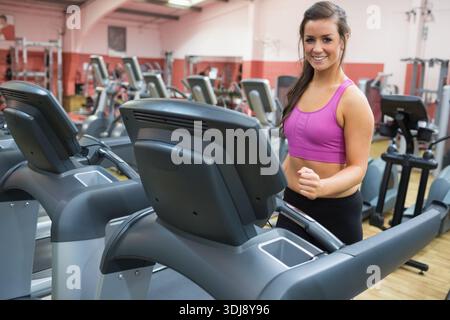 Frau, die auf der Laufbandkonsole im Fitnessstudio joggt, trägt einen pinken Sport-BH und schwarze Leggings, Kopierraum. Cardio, Geräte, Fitness, Training, Fokus, Motivation Stockfoto