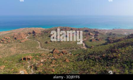 Aus der Vogelperspektive auf eine Küstenlandschaft mit felsigen Formationen, üppigem Grün und einem ruhigen blauen Ozean im Hintergrund. Sokotra, Jemen. Stockfoto