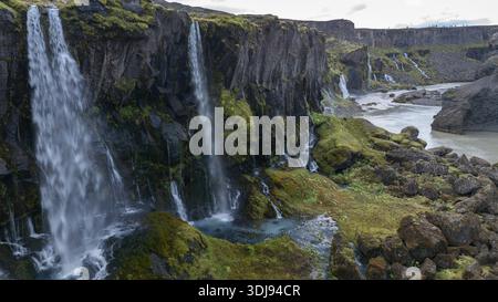 Luftaufnahme mehrerer Wasserfälle, die von einer großen Steinmauer in den Highlands, Island, ins Tal strömen Stockfoto