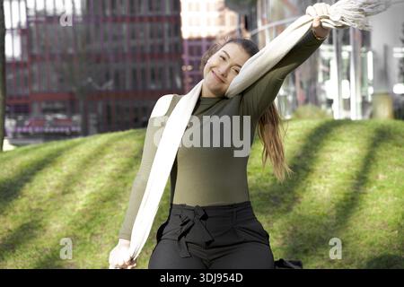 Echte Dankbarkeit, lächelnde Frau, die in einem sonnigen Park sorglos einen Schal winkt, in Hamburg, Deutschland, Stretching, Fitness, fit, sportlich, gesund Stockfoto
