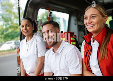 Sanitäter und Arzt im hinteren Bereich des Krankenwagens. Gruppe von drei Sanitätern, die mit Lächeln vor dem Krankenwagen stehen. Stockfoto