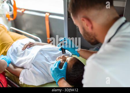 Close-up Portraitaufnahme eines ernsthaften und fokussierten Sanitäters in einem Krankenwagen mit einem verletzten Patienten. Der Medizinische Notfalltechniker Verwendet Stethosco Stockfoto
