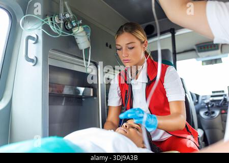 Notärzte oder Sanitäter arbeiten mit einer älteren Patientin zusammen, während er in einem Krankenwagen auf einer Liege liegt. Stockfoto