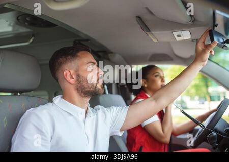 Zwei Sanitäter vor einem Krankenwagen. Der Fokus liegt auf dem Mann, einem jungen Mann im Alter von 20 Jahren, der durch das offene Fenster auf der Fahrerseite schaut. Stockfoto