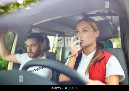 Zwei Sanitäter in Krankenwagen. Rettungssanitäterin fährt Krankenwagen, spricht über das Radio. Dringende Situation Stockfoto