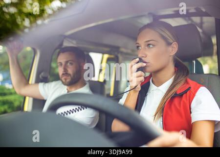 Zwei Sanitäter in den Krankenwagen. Rettungssanitäterin fährt Krankenwagen, spricht über das Radio. Dringende Situation Stockfoto