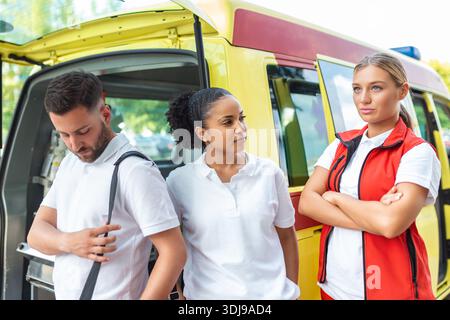 Sanitäter und Arzt stehen hinter dem Krankenwagen. Der Arzt trägt einen medizinischen Traumabeutel. Gruppe von drei Sanitätern, die vor dem Krankenwagen stehen Stockfoto