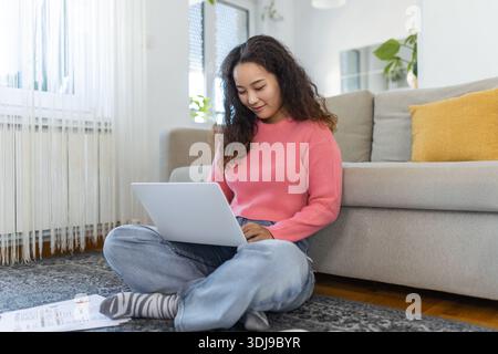 Asiatische Frau, die mit Computer auf dem Sofa sitzt, zu Hause studiert, E-Learning und freiberufliches Jobkonzept Stockfoto