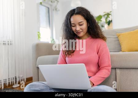 Asiatische Frau, die mit Computer auf dem Sofa sitzt, zu Hause studiert, E-Learning und freiberufliches Jobkonzept Stockfoto