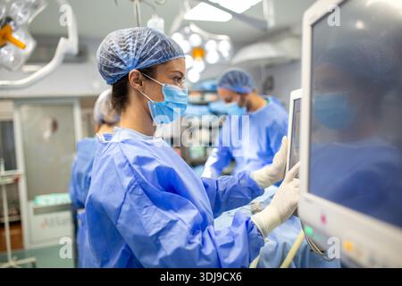 Anästhesiologe-Überwachung der Vitalparameter des Patienten während der Operation im OP. Fokussierte Ärztin mit Anästhesie-Monitoring-Geräten zur ENS Stockfoto
