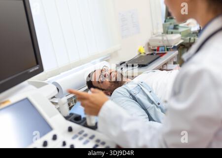 Geschickter Sonograf mit Ultraschallgerät bei der Arbeit. Mann, der seinen Arzt zur Ultraschalluntersuchung besucht. Professionelle ärztliche Sonografin im Auftritt Stockfoto
